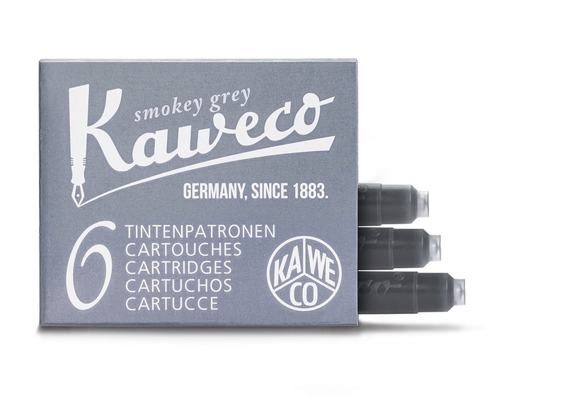May include: A box of Kaweco smokey grey ink cartridges. The box is gray with white text and a pen nib logo. The text includes "GERMANY, SINCE 1883." and the number "6". Three cartridges are visible.
