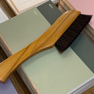 May include: A wooden brush with black bristles, resting on top of a stack of green and gray planners. The planners have the words "To Do", "Weekly", and "Planner" printed on them.