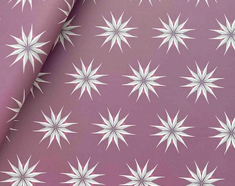 May include: A sheet of wrapping paper featuring a repeating pattern of twelve-pointed star shapes in white and light gray with small magenta accents at the center, all set against a solid, muted mauve-colored background surface.