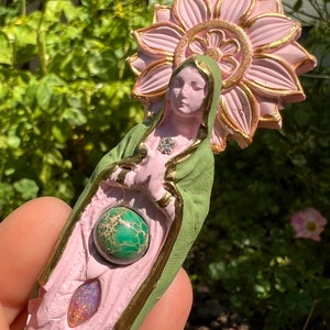 May include: A pink and green figurine of a woman with a flower halo. The figurine has a green gemstone in its hands and a pink gemstone in its lap.