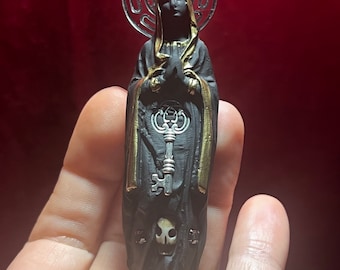 May include: Black and gold figurine of a robed figure holding a key. The figure has a skull on its chest and a halo above its head.