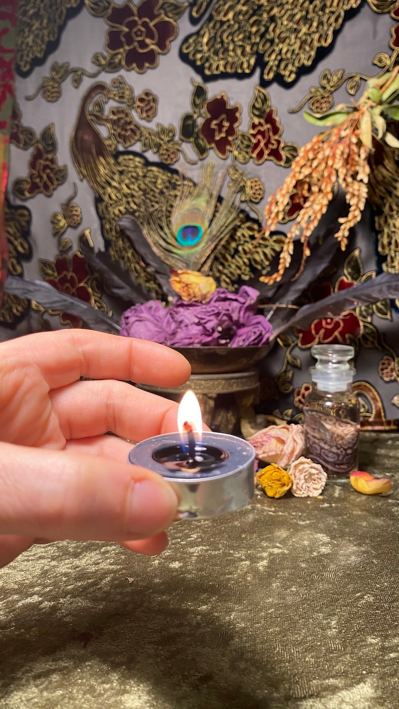 May include: A silver tea light holder with a lit candle on a green velvet surface. The candle is surrounded by dried flowers and a small glass bottle.