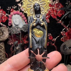 May include: Black figurine of a woman with a gold halo and a black apple in her hands. The figurine is standing on a gold base with a black star.