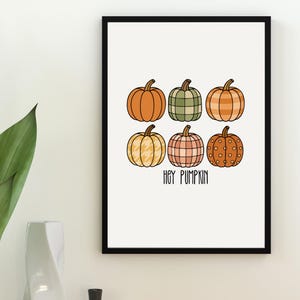 May include: A framed print with six illustrated pumpkins in shades of orange, green, and pink, each with a different pattern. The text "HEY PUMPKIN" is written below the pumpkins. The artwork is set against a white background, perfect for autumn decor.