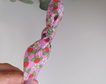 May include: Pink headband with a bow made of pink fabric with a strawberry and flower print.