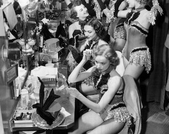 May include: A group of women in a dressing room, wearing sequined costumes and hats. Some are applying makeup while others are looking in the mirror.