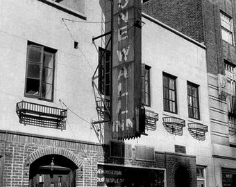 May include: Black and white photograph of the Stonewall Inn, a historic bar. The sign reads "Stonewall Inn" vertically. The building has a brick facade and arched doorway. A sign below the windows reads "WE HOMOSEXUAL... CONDUCT ON THE VILLAGE."
