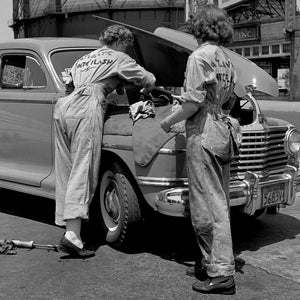 May include: Two women in denim overalls are working on a vintage car with the hood open. The car is a light-colored sedan with a chrome bumper and a license plate that reads "5683Y". The women are wearing work shirts with the text "Atlantic Refining Company" printed on them.