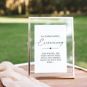 May include: A framed sign with gold trim and a white insert. The text on the insert reads "In loving memory" in elegant script, followed by a message. The sign is on a wooden tray with a peach-colored cloth.