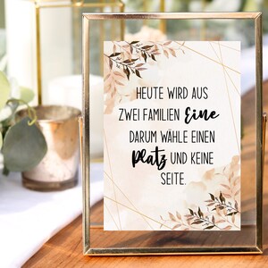 May include: A gold-framed sign with a watercolor background and gold geometric shapes. The sign reads "Heute wird aus zwei Familien eine darum wähle einen Platz und keine Seite."