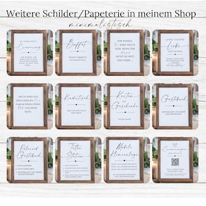 May include: A collection of framed signs with brown wooden frames and white backgrounds. The signs feature black calligraphy text in German, with phrases like "Buffet," "Guestbook," and "Tattoo Station." The signs are arranged in a grid.
