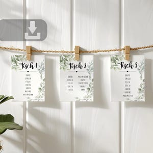 May include: Three white table cards with names, labeled "Tisch 1", "Tisch 2", and "Tisch 3", are suspended from a rope with wooden clips. Each card has a botanical border and a list of names.