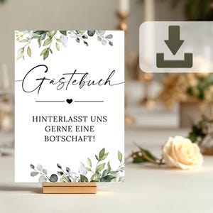 Könnte beinhalten: Ein weißes Schild mit grünen und weißen floralen Akzenten. Das Schild sagt "Gästebuch" und "Hinterlasst uns gerne eine Botschaft!"