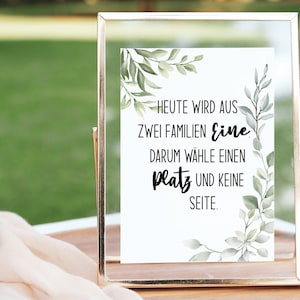 Könnte beinhalten: Ein weißes Schild mit grünen, blättrigen Zweigen oben und unten. Das Schild lautet "Heute wird aus zwei Familien eine. Darum wähle einen Platz und keine Seite."