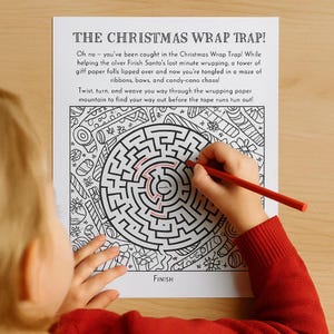 Op de afbeelding: Een zwart-wit kerstthema doolhof met de tekst "THE CHRISTMAS WRAP TRAP!". Een kinderhand gebruikt een rode potlood om een pad te traceren. Het woord "FINISH" staat onderaan.