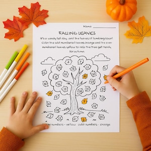 Puede incluir: Una mano infantil coloreando una hoja de actividades "Falling Leaves" con un rotulador naranja. La hoja presenta un árbol con hojas numeradas, instrucciones y decoraciones con temática otoñal.