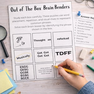 May include: A printed puzzle sheet titled "Out of The Box Brain Benders" with word puzzles. The sheet includes boxes with phrases and visual clues. A hand holds a pencil, pointing at a puzzle. An answer key is visible.