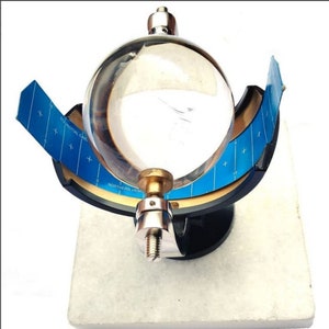 May include: A clear glass globe sits in a black metal stand with a blue and white grid pattern. The stand is labeled "NORTHERN HEMISPHERE" and "EQUATORIAL ZONE".