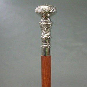 May include: A silver-colored walking cane with a decorative floral design on the handle and a polished wooden shaft. The top of the handle is round and the shaft is a reddish-brown color.