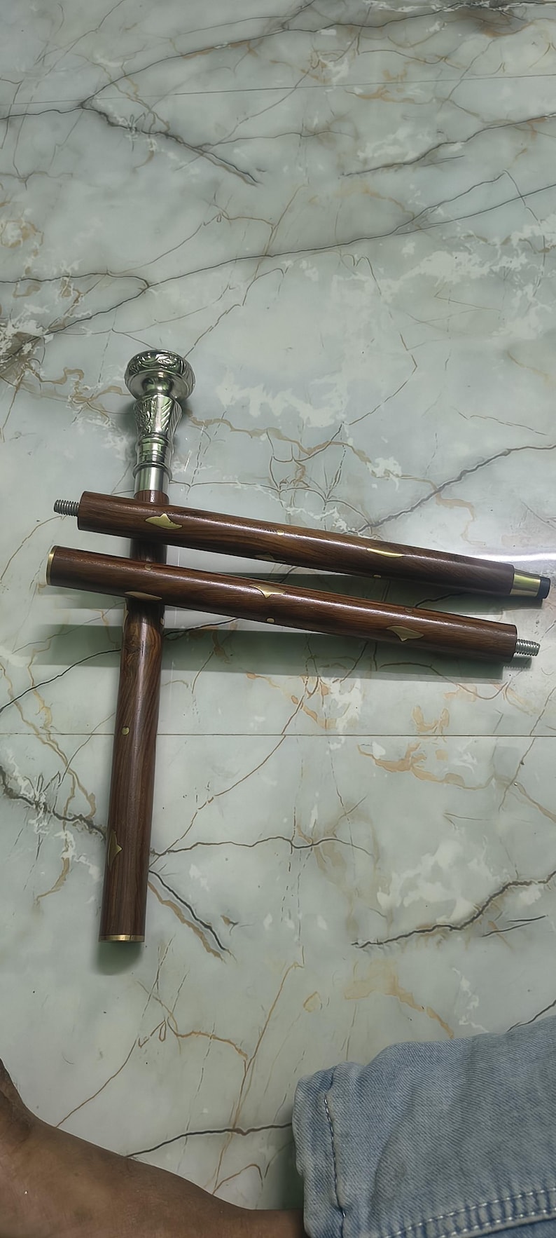 May include: A wooden walking cane with a silver-colored handle and decorative brass accents. The cane is brown with a dark finish and has a screw-on design for easy assembly. The cane measures approximately 36 inches in length.