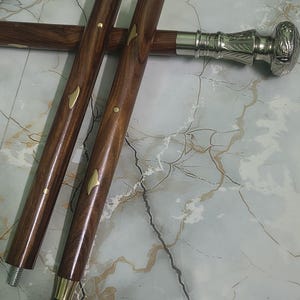 May include: A wooden walking cane with a decorative silver handle and brass accents. The cane's shaft is a rich brown color, and the handle features intricate carvings. The cane is approximately 36 inches long.
