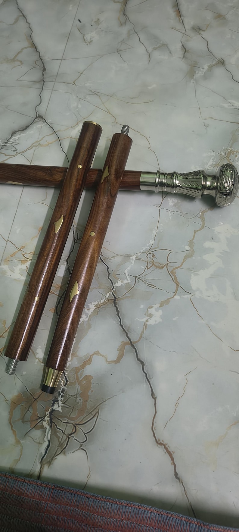 May include: A wooden walking cane with a decorative silver handle and brass accents. The cane's shaft is a rich brown color, and the handle features intricate carvings. The cane is approximately 36 inches long.
