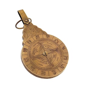May include: A brass compass with a circular face featuring zodiac symbols and a calendar. The compass has a decorative floral design and a ring for hanging.