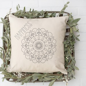 May include: A white cushion with a black mandala design and the word "Happiness" printed on it. The cushion is surrounded by a green garland.