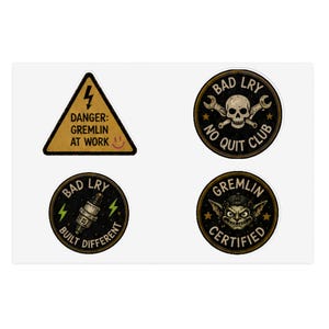 May include: A set of four stickers featuring a yellow triangular warning sign with the text DANGER: GREMLIN AT WORK, a circular badge with a skull and wrenches labeled BAD LRY NO QUIT CLUB, a spark plug icon, and a gremlin face labeled GREMLIN CERTIFIED.