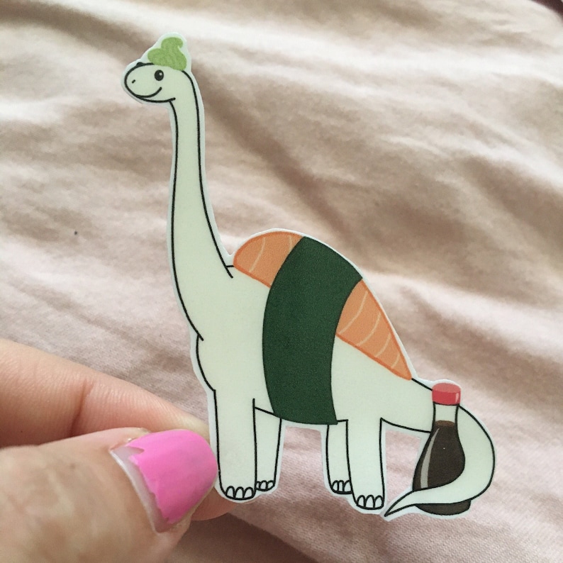 May include: A white dinosaur with a green seaweed hat is dressed as a sushi roll with a salmon filling. The dinosaur is holding a small bottle of soy sauce.