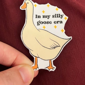 May include: A white goose sticker with orange feet and a yellow beak. The sticker has the text "In my silly goose era" with yellow stars around the text.