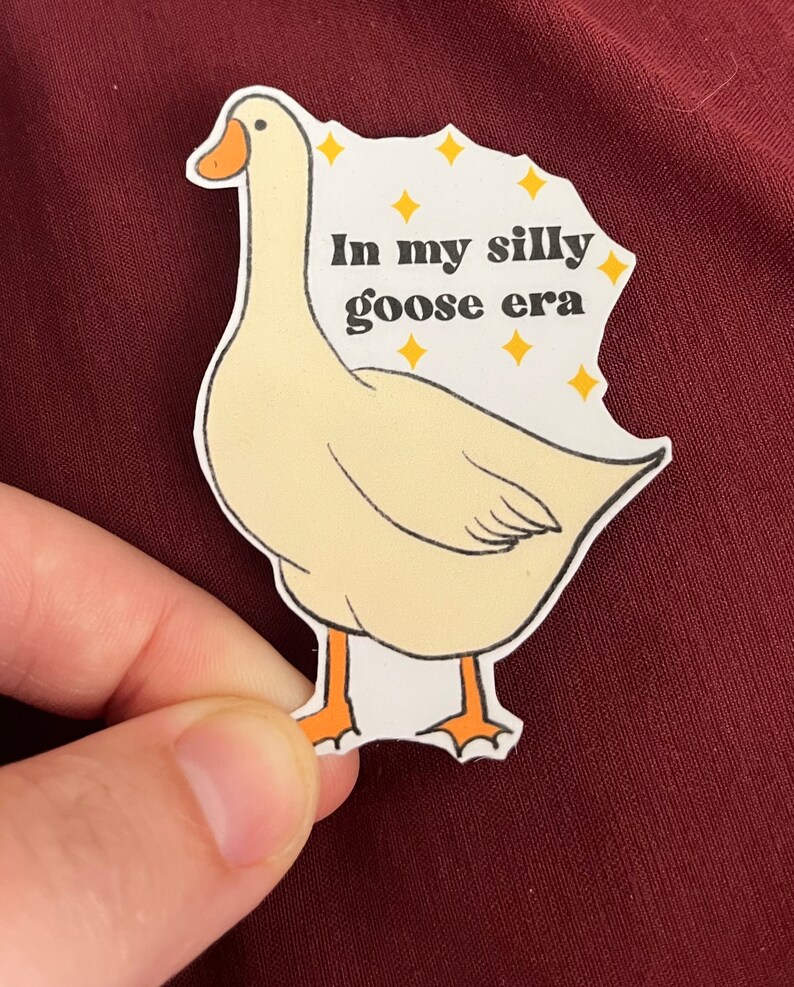 May include: A white goose sticker with orange feet and a yellow beak. The sticker has the text "In my silly goose era" with yellow stars around the text.