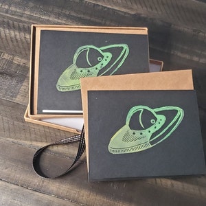 May include: Two black cards with a green and black alien spaceship design. The cards are blank and ready for writing.