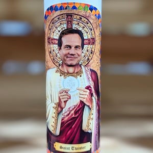 May include: A white candle with a colorful image of a man holding a communion wafer. The image is surrounded by a gold frame and the text "Saint Twister" is printed below the image.