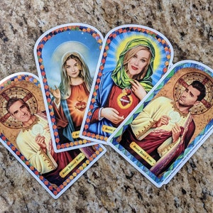 May include: Four colorful illustrated cards with a religious theme. Each card features a different person with a halo and a name at the bottom. The cards are decorated with gold accents and floral patterns.