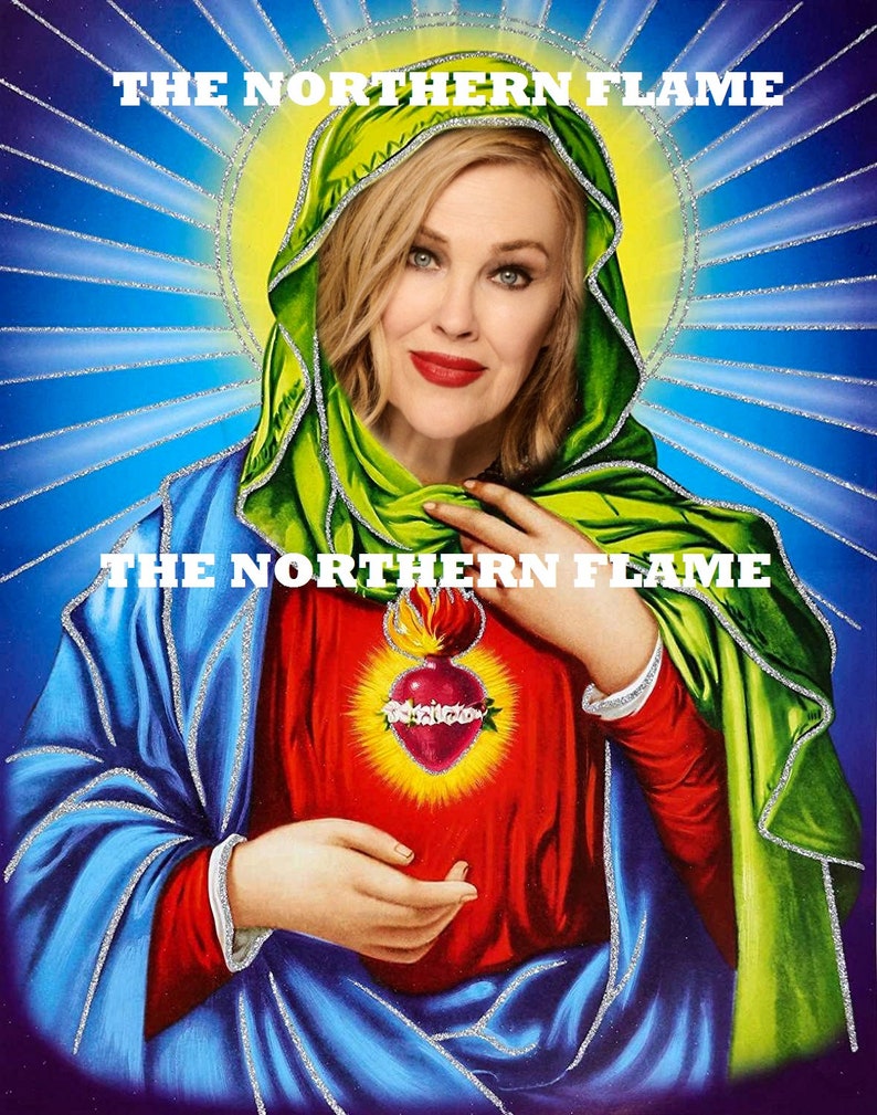 May include: A digital art print of a woman with blonde hair wearing a green and blue robe. The woman is holding a red heart with flames on top. The text "THE NORTHERN FLAME" appears twice on the image.