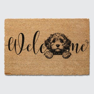May include: A brown coir doormat with the word "welcome" in black cursive script. A black and white illustration of a dog's head peeking out from behind the word "welcome".