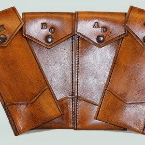 May include: Four brown leather cases with initials embossed on the front. The cases are arranged in a semi-circle with the initials facing the viewer. The initials are "JH", "BO", "AD", and "GR".