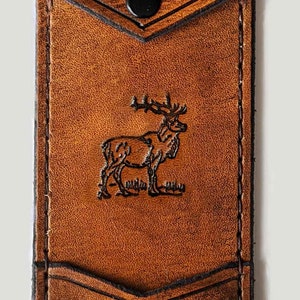 May include: A brown leather wallet with a flap closure and a snap button. The wallet has a pocket on the front and a deer silhouette embossed on the front. The initials "E.G." are embossed on the top flap.