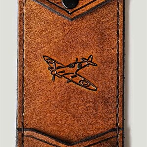 May include: A brown leather wallet with a flap closure and a snap button. The wallet has a pocket on the front with the initials "E.G." embossed on it. A small airplane is embossed on the front of the wallet.
