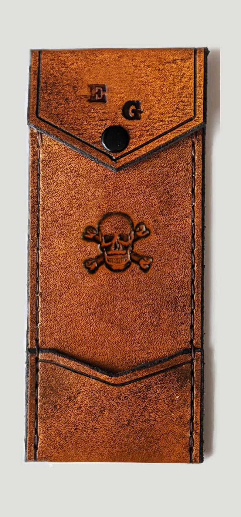 May include: A brown leather wallet with a skull and crossbones design and the initials "E.G." embossed on the front.