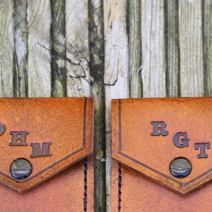 May include: Two brown leather pouches with metal snaps. The pouch on the left has the initials "OHM" embossed on the front. The pouch on the right has the initials "RGT" embossed on the front.