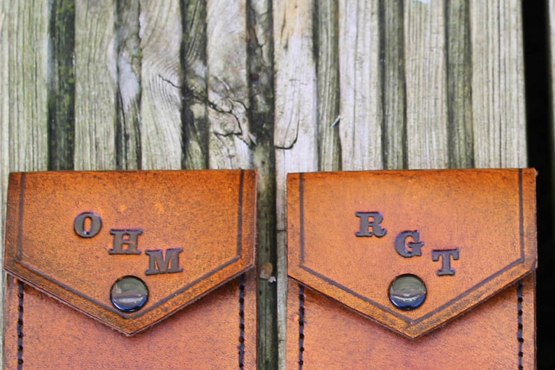 May include: Two brown leather pouches with metal snaps. The pouch on the left has the initials "OHM" embossed on the front. The pouch on the right has the initials "RGT" embossed on the front.