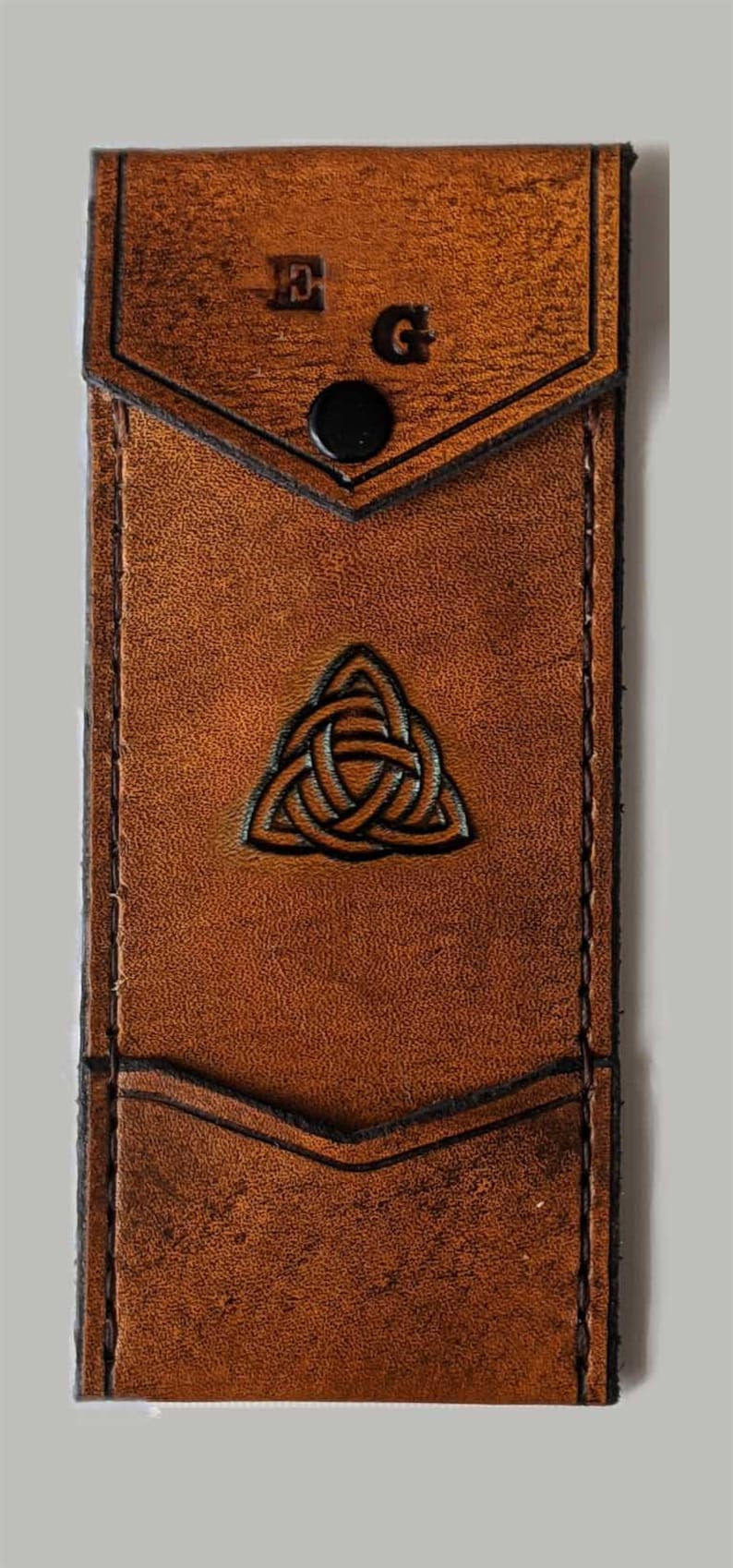 May include: A brown leather wallet with a Celtic knot design and the initials "E.G." embossed on the front.
