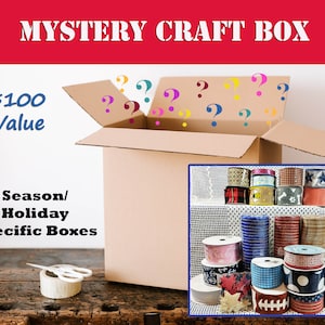May include: A brown cardboard box with the words "MYSTERY CRAFT BOX" printed on the top. The box is open and there are question marks inside. The text "$100 Value" is printed on the side of the box. The text "Season/Holiday Specific Boxes" is printed below the box. A roll of tape and scissors are on a wooden surface in front of the box. A variety of colorful ribbons are shown in the background.