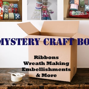 May include: A brown cardboard box with the text "MYSTERY CRAFT BOX" printed on the front. The box is open and contains a variety of colorful ribbons, wreath making supplies, and embellishments. The text on the box also reads "Ribbons, Wreath Making, Embellishments & More".