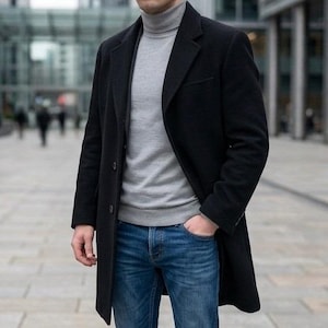 May include: A black overcoat worn over a light gray turtleneck sweater and blue denim jeans. The overcoat features a notched lapel, long sleeves, and a button-front closure. The sweater has a high neck, and the jeans have a classic blue wash.