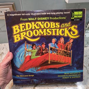 May include: A square Disneyland Record album cover for Bedknobs and Broomsticks featuring a colorful illustration of four people riding a flying brass bed over a blue swirling background. The text includes the title and production credits.