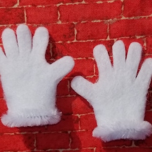 Könnte beinhalten: Zwei weiße Filzhandschuhe mit einem flauschigen weißen Besatz. Die Handschuhe liegen auf einem roten Ziegelmuster-Hintergrund.