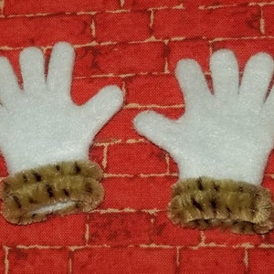 Könnte beinhalten: Ein Paar weiße Filzhandschuhe mit braunen Kunstfellmanschetten. Die Handschuhe liegen auf einem roten Ziegelhintergrund.